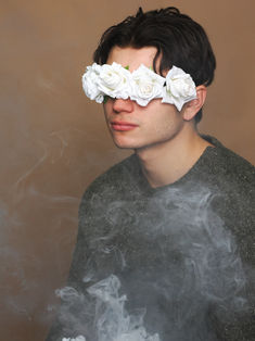Photo book de Rémi Chabanel, mannequin & musicien, réalisée en studio sur fond marron. Le modèle, habillé d’un pull vert, porte un bandeau de roses blanches sur les yeux, créant un effet visuel doux et mystérieux. Entouré de fumée, l’atmosphère de l’image est à la fois romantique et énigmatique, ajoutant une touche de poésie à l’ensemble. Une photo élégante et originale, idéale pour un portfolio mettant en avant le côté artistique et expressif du modèle.