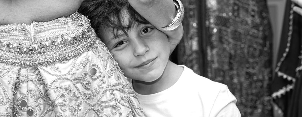Portrait en noir et blanc d’un jeune garçon souriant, lové contre une invitée en tenue traditionnelle brodée, capturé lors du mariage kurde-tunisien d’Omer et Syrine par Colombe Photographie.