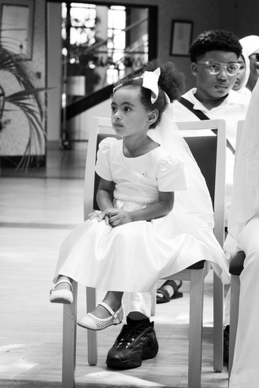 Photographie en noir et blanc d’une fillette vêtue de blanc lors du mariage civil de Malika et Richard à Guyancourt, en Île-de-France. Reportage mariage sensible et naturel capturé par Colombe Delons, photographe de mariage en région parisienne.