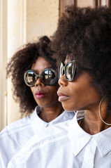 Portrait mode éditorial de Nina & Paco, sœurs, dans les rues de Paris. Elles portent des lunettes de soleil, une chemise blanche et ont les cheveux détachés, affichant un style moderne et sophistiqué. Cette image illustre les avantages d’une séance photo en extérieur, mettant en valeur l’élégance urbaine et la spontanéité d’un duo complice dans un décor parisien emblématique.