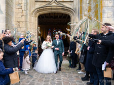 Photographie des mariés sortant de l'église, entourés d'une haie d'honneur d'invités, capturée après la cérémonie religieuse en région parisienne. Un moment de joie et d'émotion, immortalisé par Colombe Delons, photographe spécialisée dans les mariages et les instants authentiques de votre grand jour.