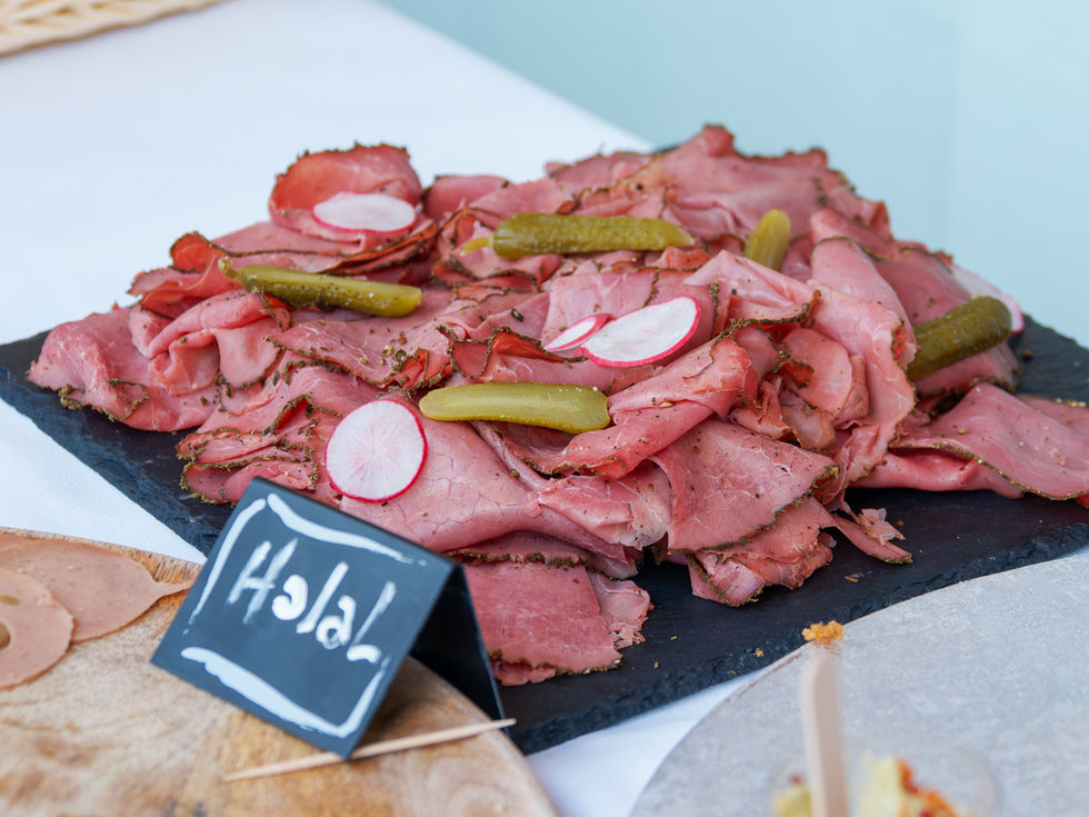 Photographie culinaire réalisée par Colombe Photographie à Paris. Gros plan sur un plateau de charcuterie halal, composé de fines tranches de viande assaisonnée, garnies de rondelles de radis et de cornichons, disposé sur une ardoise noire. Ce type de présentation illustre le savoir-faire des traiteurs et l’élégance d’un buffet. Photographe culinaire à Paris et en Île-de-France, je réalise des shootings professionnels pour valoriser les plats et préparations gastronomiques des chefs et traiteurs.