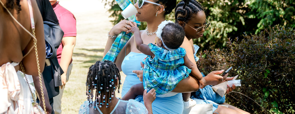 Scène de mariage capturée en extérieur à Dammarie-lès-Lys, montrant une invitée assise avec deux enfants dans une ambiance familiale et détendue. Un instant volé plein de tendresse, immortalisé par Colombe Photographie, photographe de mariage en Île-de-France, spécialisée dans les photos prises sur le vif à Gentilly, Paris et alentours.