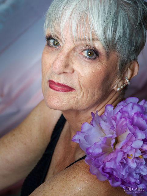 Portrait réalisé en studio par Colombe Photographie dans le cadre d’un shooting baignoire fleurie avec Monique. La mise en valeur de son regard lumineux, de ses cheveux argentés et du contraste avec une grande fleur violette illustre l’art du portrait photographique professionnel. Photographe portraitiste à Gentilly et en région parisienne, je capture des portraits artistiques et authentiques qui révèlent la personnalité et la beauté de chaque modèle, quel que soit l’âge.