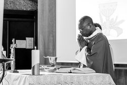 Photographie en noir et blanc d’un prêtre en prière devant l’autel pendant une messe de première communion, mains jointes et yeux fermés, dans une église baignée de lumière. Cette image a été prise à la paroisse Notre-Dame du Sacré-Cœur de Coeuilly. Photographe professionnelle d’événements religieux à Gentilly et en Île-de-France, je saisis l’émotion et la spiritualité de vos célébrations.