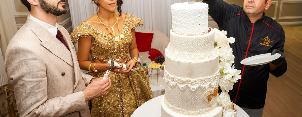 Moment de la découpe du gâteau de mariage à plusieurs étages, les mariés en tenues dorées observant le pâtissier, photo réalisée par Colombe Photographie lors du mariage kurde-tunisien d’Omer et Syrine à Saint-Gratien.