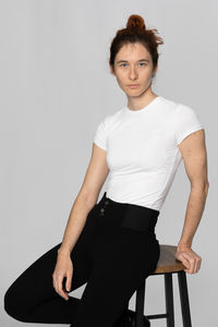 Portrait Polaroid de Romane RENAUD, mannequin, réalisé en studio sur fond blanc. Elle est assise sur un tabouret, le visage tourné vers la caméra avec un air neutre. Romane porte un jean noir et un t-shirt blanc à manches courtes, cheveux attachés. Cette image met en avant l'impact d'une séance photo en studio pour des portraits de mannequin, avec un éclairage maîtrisé et un fond épuré qui permet de concentrer l'attention sur le modèle.