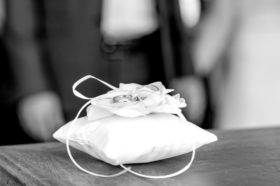Photographe de mariage à Paris – détail des alliances de Daniela et David posées sur un coussin blanc, prêtes pour l’échange des vœux à la mairie du 9ème arrondissement. Ce cliché en noir et blanc capture l’élégance et la symbolique du mariage civil, avec le coussin orné d’un ruban et d’une fleur en tissu. Un instant délicat et intemporel qui illustre l’importance des détails dans un reportage de mariage. Colombe Photographie, photographe de mariage en région parisienne, Gentilly et Île-de-France, immortalise avec sensibilité chaque moment clé.