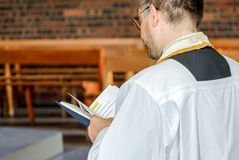 Prêtre en habit liturgique tenant un livre de messe pendant le baptême de Giulia à l’église Sainte Geneviève de Garges-lès-Gonesse. Reportage réalisé par une photographe baptême à Paris et en Île-de-France, capturant les moments clés de la cérémonie religieuse en famille.