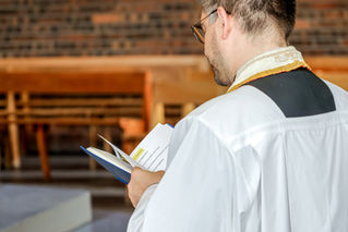 Prêtre en habit liturgique tenant un livre de messe pendant le baptême de Giulia à l’église Sainte Geneviève de Garges-lès-Gonesse. Reportage réalisé par une photographe baptême à Paris et en Île-de-France, capturant les moments clés de la cérémonie religieuse en famille.