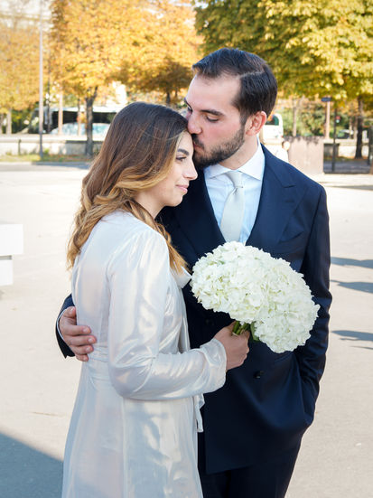 Photo couleur d’Annapaola et Angelo juste après leur mariage civil à la mairie du 7e arrondissement de Paris. Le marié embrasse tendrement le front de son épouse, qui tient un bouquet d’hortensias blancs. Cette scène intime et lumineuse illustre la douceur et la complicité du couple, photographiée par Colombe Photographie, photographe de mariage civil à Paris et en région parisienne.