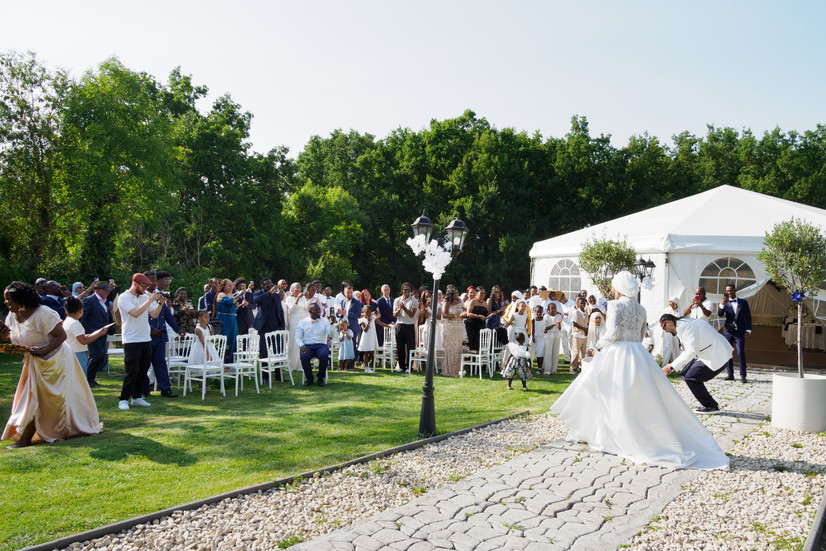 Photo du mariage de Malika et Richard à Guyancourt : les mariés font leur entrée sous les acclamations des invités, dans un cadre verdoyant et festif. Reportage photo de Colombe Delons, photographe de mariage en région parisienne.