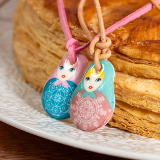 Photographie culinaire mettant en scène des fèves Matriochka en porcelaine autour d’une part de galette des rois, avec une lumière douce pour sublimer les détails