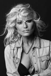 Portrait en noir et blanc d'Alexia VIC, mannequin, réalisé en studio sur fond noir. Ses cheveux sont au vent, et elle regarde intensément vers la caméra. Elle porte une veste en jean entrouverte, ajoutant une touche de caractère et d'élégance. Cette image illustre les avantages d'une séance photo en studio, où le contrôle de la lumière et du contraste met en valeur les expressions et la profondeur d'un portrait féminin artistique et intemporel.