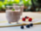 Glas mit Smoothie, daneben Blau- und Himbeeren