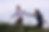 A couple joyfully runs through tall grass in a field, the man leading the woman. The sky is overcast, creating a serene, playful mood.