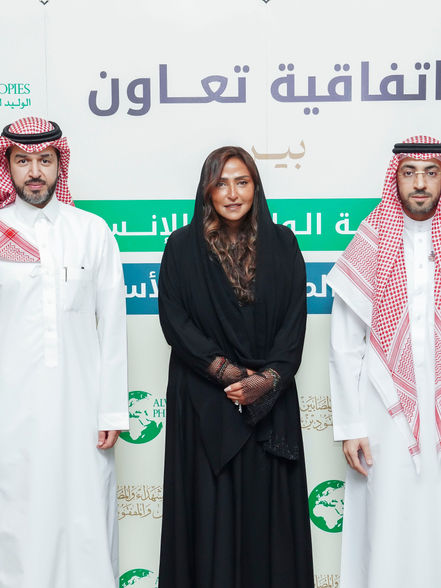 Two men and a woman stand in front of a cooperation agreement sign.