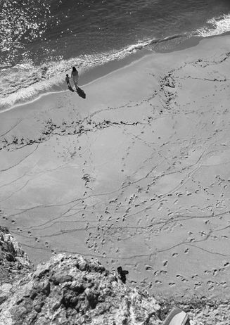 vue contre plongée de la plage, il y a une femme sui tient la main d'une jeune fille, elles ont toutes els deux les pieds dans l'eau.