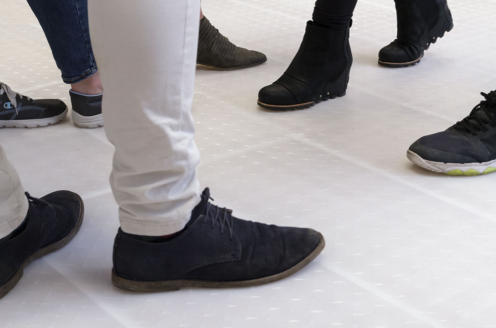 Multiple pairs of feet wearing various shoes on a patterned floor.