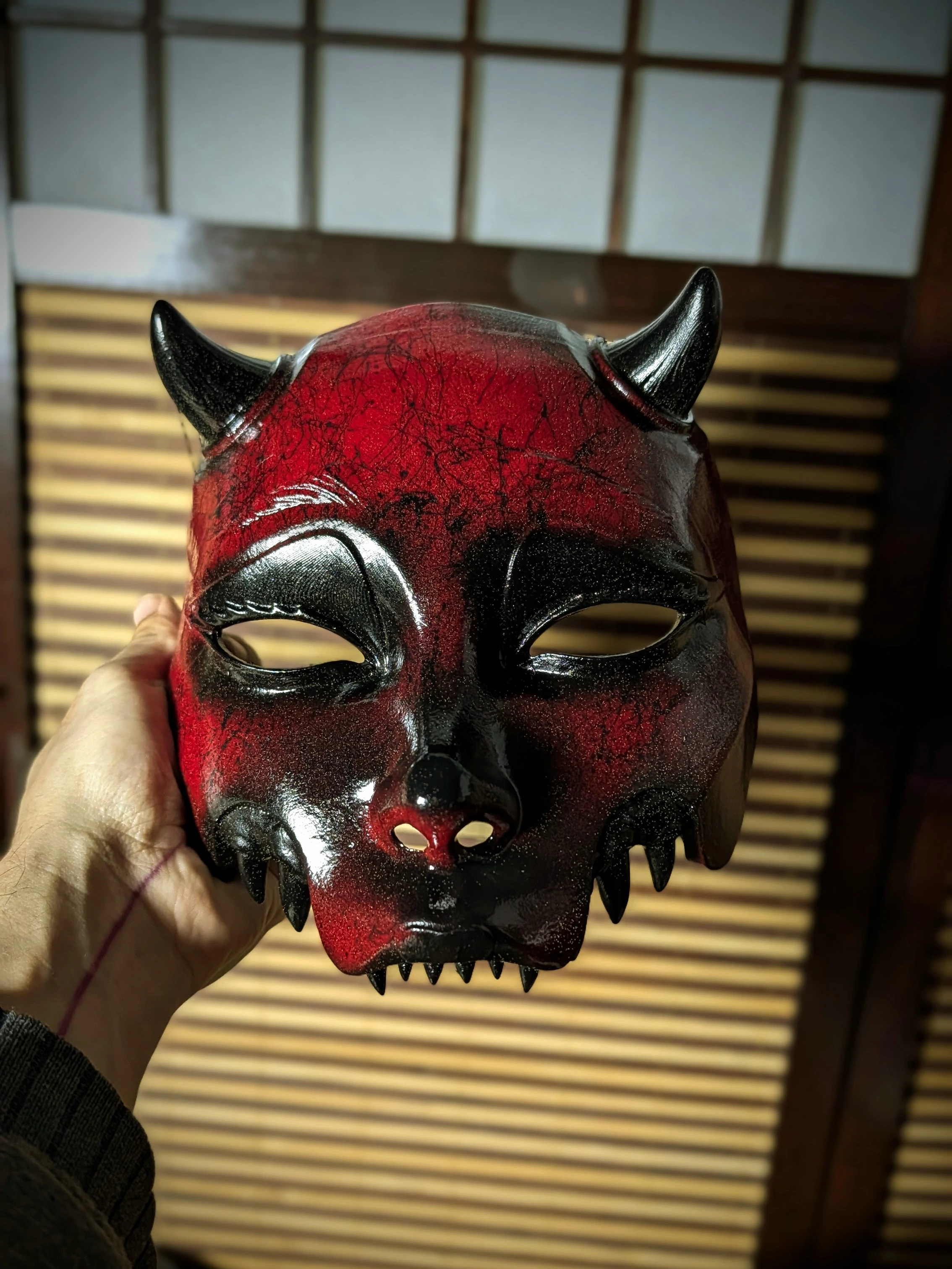 Handmade red and black Mempo Oni half-mask with horns, crafted from PETG by Dai Yokai, in a Japanese demon style, perfect for cosplay or wall decoration.