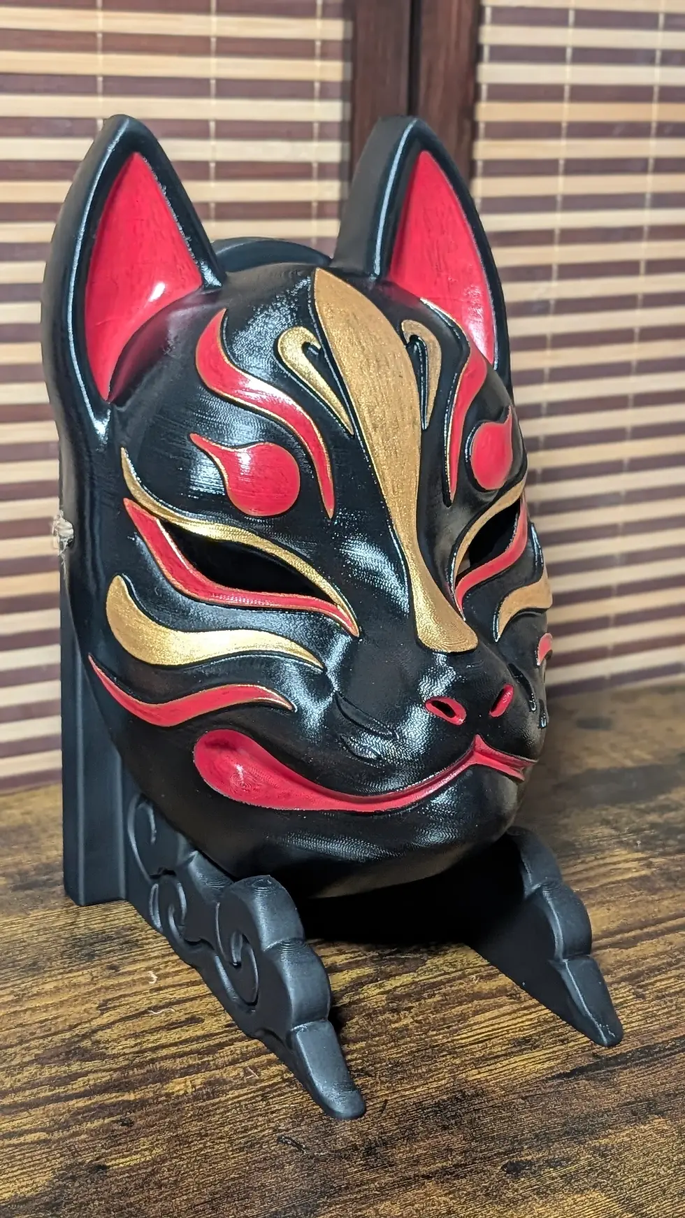 Miniature : Masque Kitsune noir moderne sur stand, marquages or et rouge peints à la main, vue de profil, Dai Yokai Bretagne