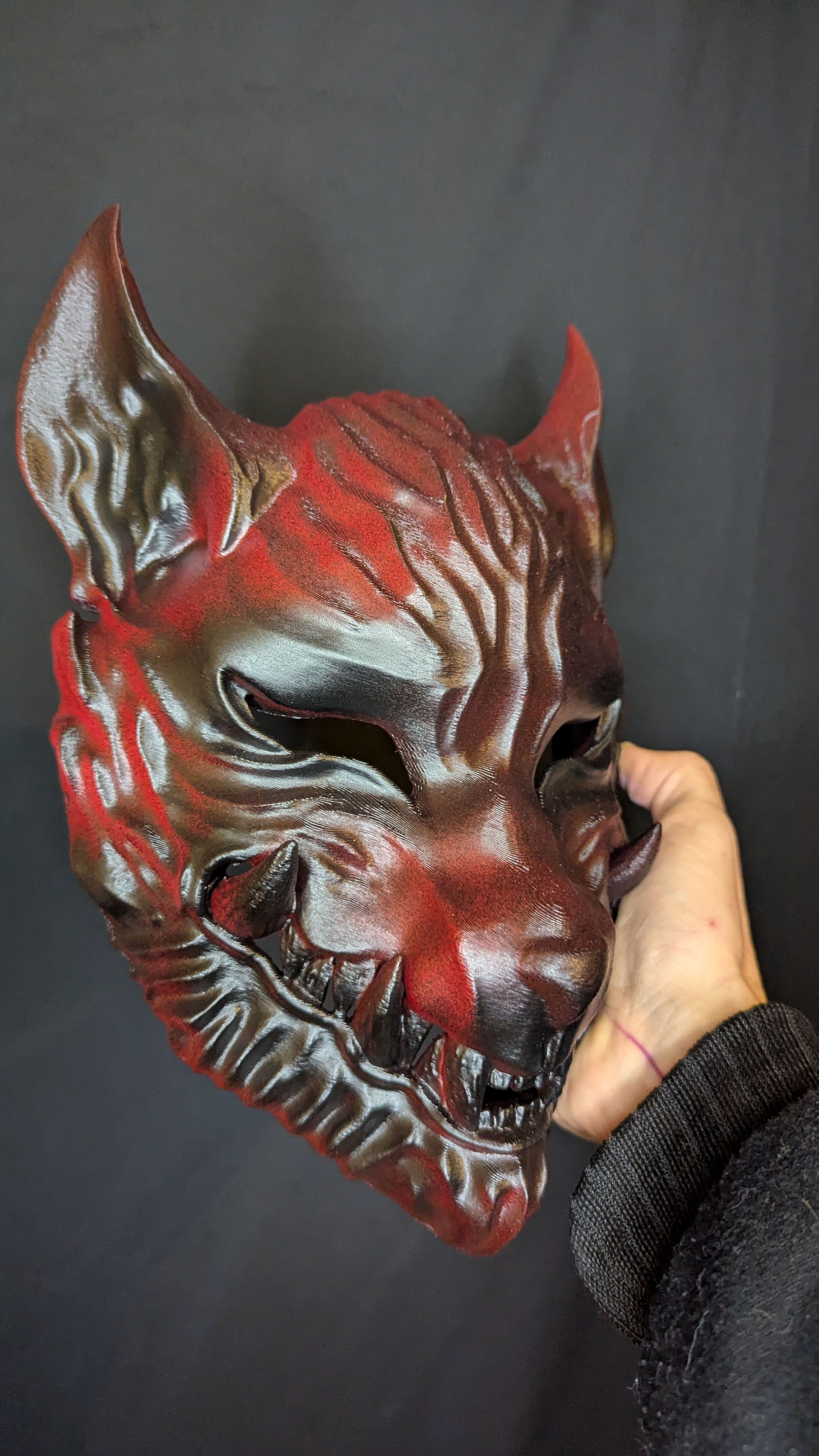 Rot-schwarze Ōkami-Wolfsmaske von Dai Yokai, seitlich in der Hand gehalten