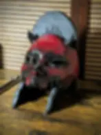 Masque Kuchisake Mempo fait main en PETG, peinture rouge craquelée sur fond noir, posé sur support mural dans l'atelier Dai Y