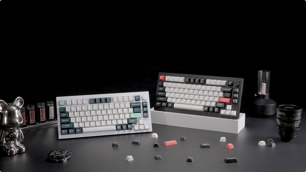 Two keyboards with mixed-color keys on a black surface. Silver bear figurine, decorative tubes, and camera lens in the background.