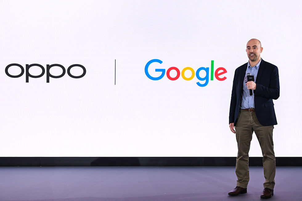 Man speaking on stage with a microphone, logos of Oppo and Google behind him on a white background. Formal attire, focused mood.