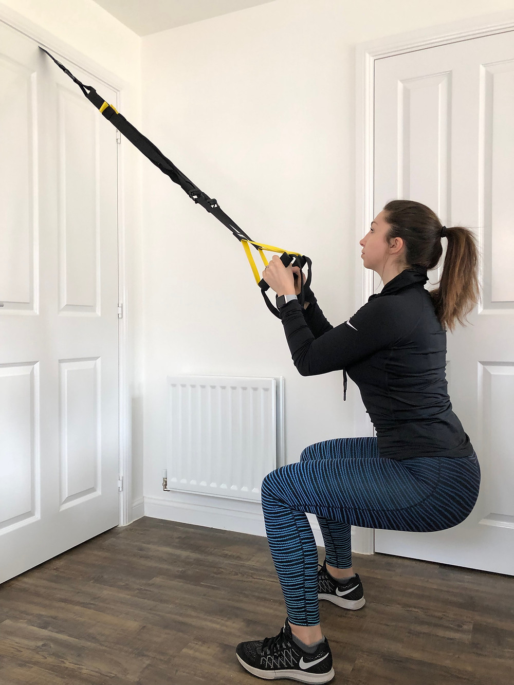 Woman performing a squat using the TRX training at home