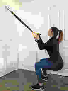Woman performing a squat using the TRX training at home