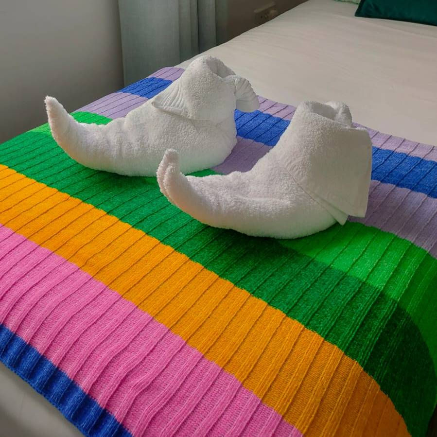 Two towel creations resembling a pair of elf shoes atop a colorful, striped blanket.