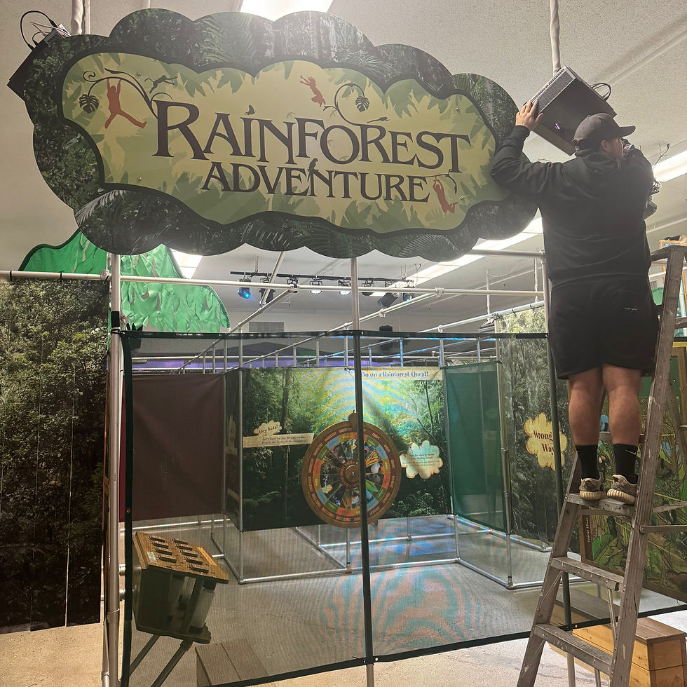 A man setting lifting a speaker to the right of a sign that reads, "Rainforest Adventure". Below is a mesh covering.