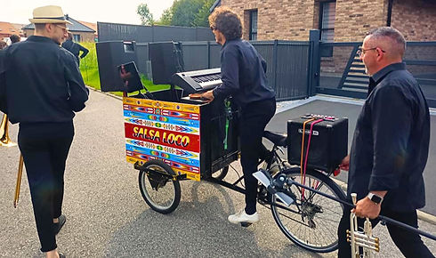 Un pianiste jouant sur un piano monté sur un vélo décoré avec le carton 'SALSA LOCO', suiv