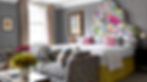 Hotel bedroom suite featuring bed with tall multicolor-floral upholstered headboard. At the end of the bed is a sofa with bold graphic black and white pattern. The wallcovering has a grey linen texture to it and there are multi striped pillows, multicolored curtains in a geometric pattern and more floral pillows on the sofa. The bedskirt is a yellow matelasse with a chevron pattern. There are some art pieces on the walls in different styles, one in a modern frame and one in a gold and black classical frame. A walnut bistro table houses a couple of side chairs with a mix of grey and bright pink upholstery. The overall feeling is cheerful but cozy.