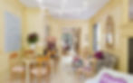 Informal sitting room with a variety of furnishings including midcentury modern dining chairs and game table, traditional style settee with graphic black and white upholstery, slope arm side chairs , a vintage bamboo chippendale chair a parsons console table and a freeform coffee table. Walls are paneled and painted in two shades of butter yellow with accents in dark plum, lavender and orchid. Floors are pale wood and a contemporary white metal candelabra sconce hangs above. A gilt mirror and some large scale original art complete the room. The overall feeling is sunny and carefree.