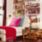Close up photo of custom Donghia chaise sitting under bookcase in above room. One pink and one turquoise pillow and one turquoise pillow add some color along with a red throw draped across the foot. A small brass reading lamp off to the side and a bamboo side table with some decor items complete this cozy little corner.