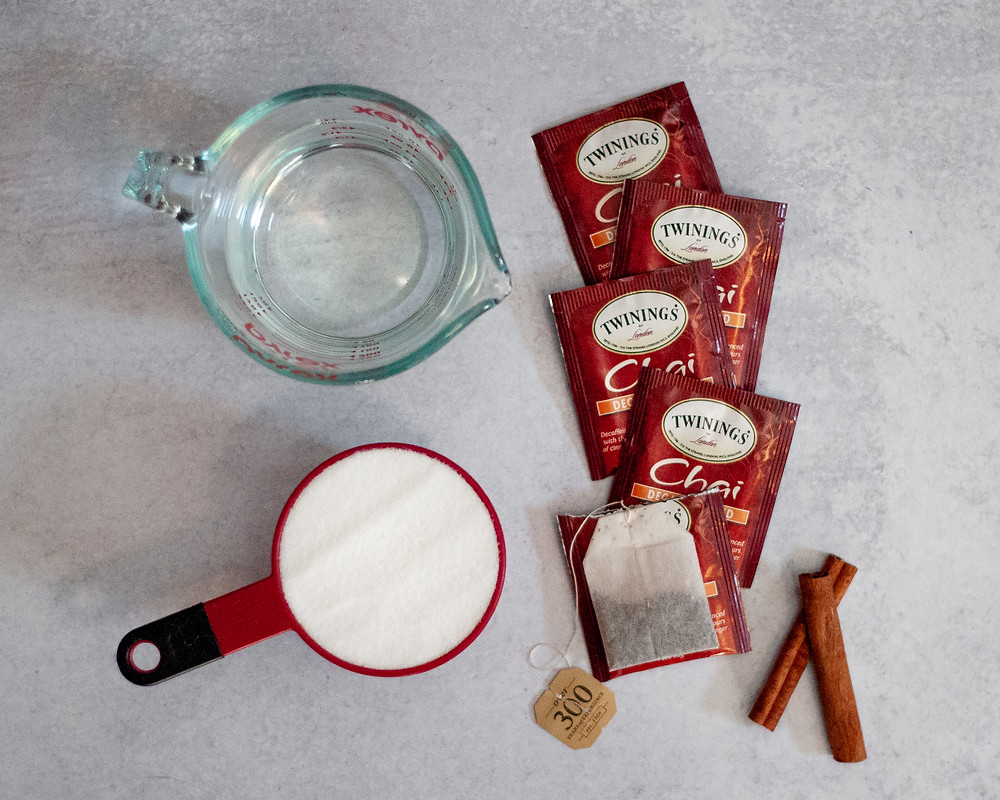 ingredient shot for this chai tea simple syrup recipe, showing water, granulated sugar, chai tea bags, and cinnamon sticks