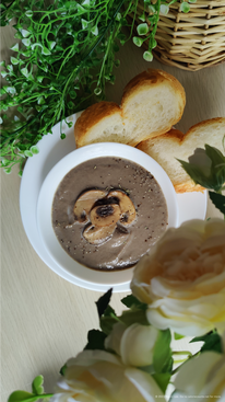 Creamy mushroom soup in a bowl topped with some mushroom slices, paired with French baguette slices.