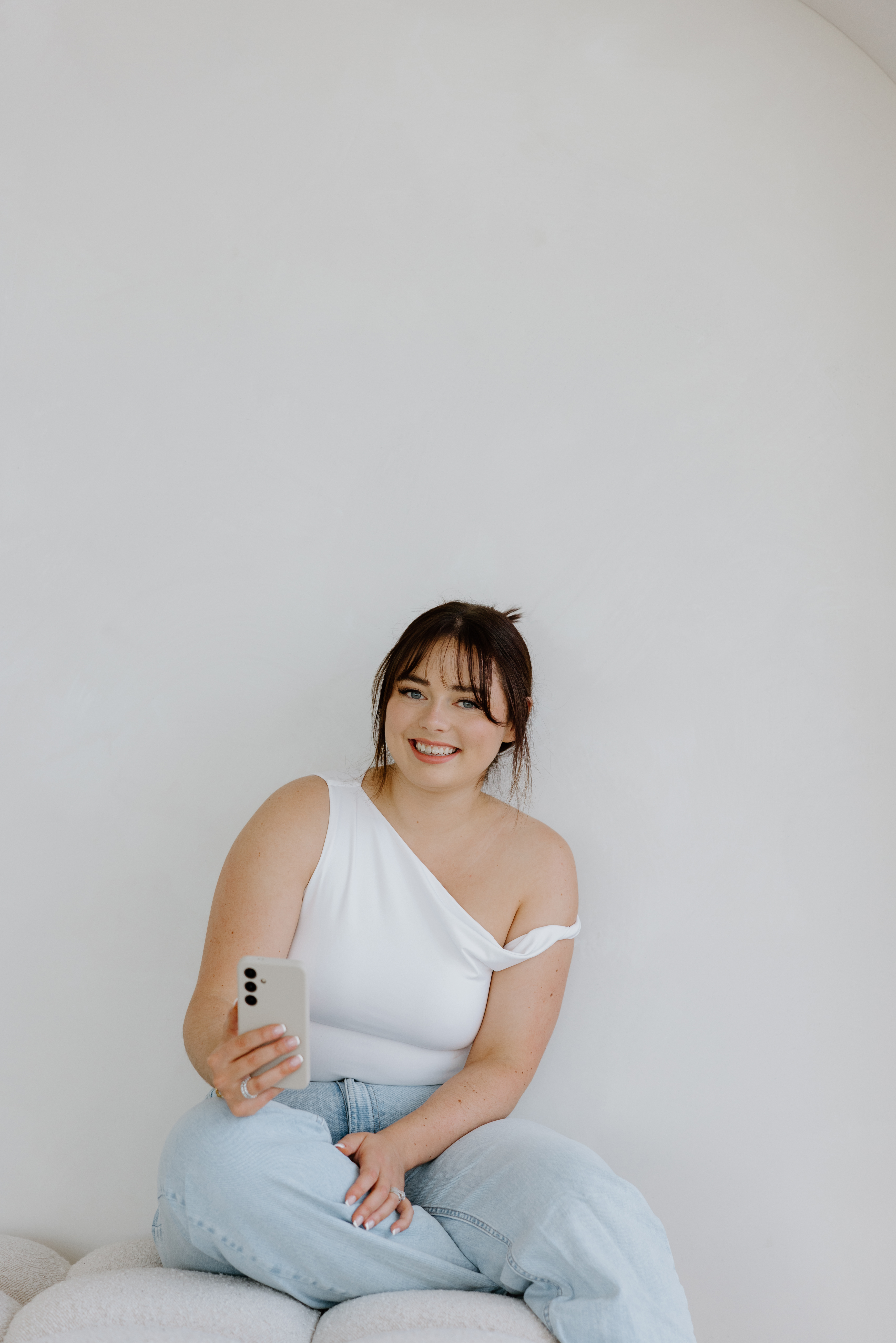 Paige, founder of Easy Peasy VA, sitting cross-legged on a couch smiling while holding her phone