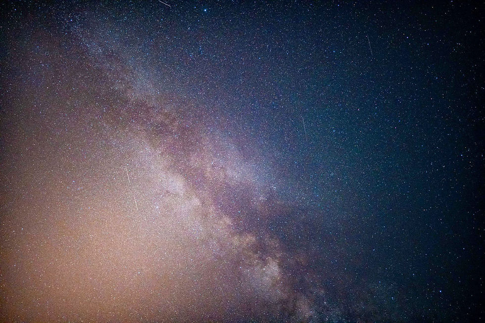 Stargazer with a red head torch watching the Milky Way and a Perseid meteor from a clifftop in Malta