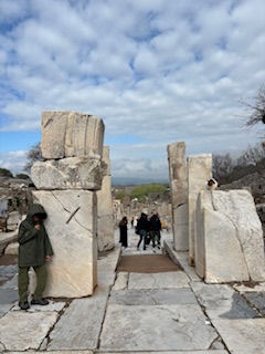 Visitors exploring ancient ruins of Ephesus, with large stone pillars marking the entrance to the commercial district.