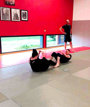 Deux personnes font des abdos sur un tapis, coach observant.