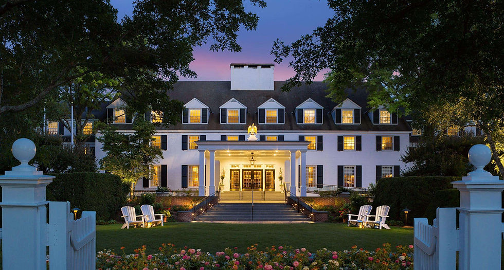 Woodstock Inn and Resort, Woodstock Vermont, lit up at dusk with white columns, manicured gardens, and Adirondack chairs lining the front entrance.
