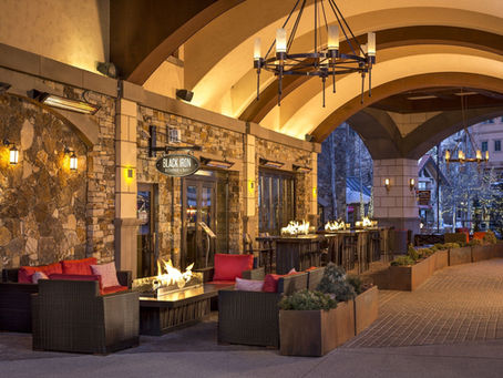 Black Iron Kitchen and Bar outdoor terrace at Madeline Hotel and Residences Auberge Collection in Telluride Colorado with stone arches fire tables and red lounge seating