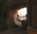 A caucasian couple sits in an archway at a table over looking Rome. In the distance the dome of the Vatican can be seen. Photo credit it Alessandro Quarta.