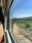 A photo of an arm leaning against a window, through the window a small town is visible in the distance. 
