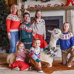 Family wearing matching Christmas sweaters posed next to an alpaca