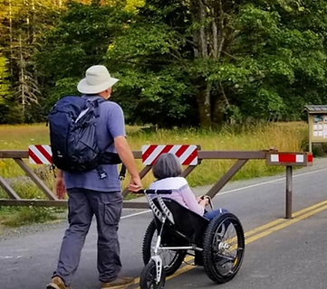 Image for article intro. Two hikers, one in a wheelchair and one walking behind, enter a gated area on a road.