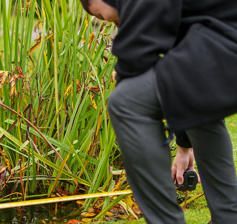 Person measuring a garden pond with a yellow tape measure.